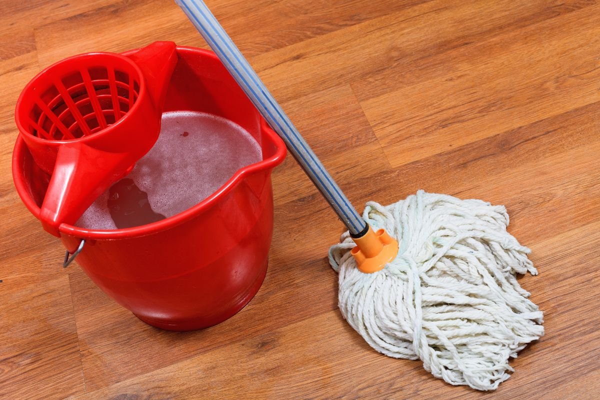 A mop and bucket placed on a polished wooden floor, ready for cleaning tasks.